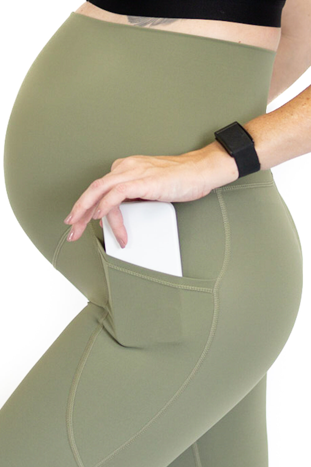 Pregnant woman’s torso in olive green maternity leggings with pockets for comfort