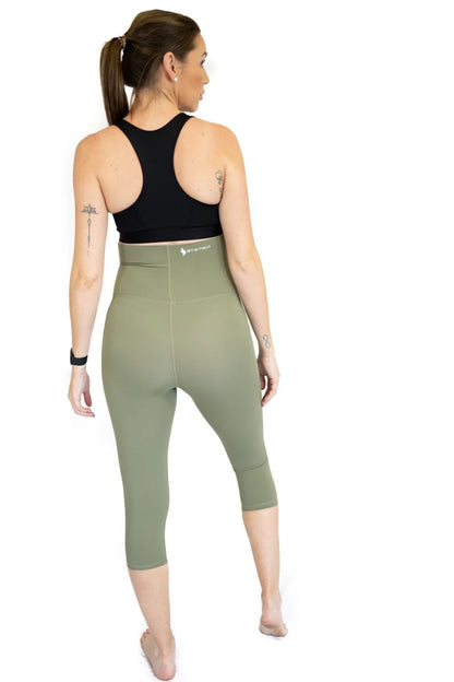 Woman in black sports bra and olive maternity leggings from behind, showcasing pockets