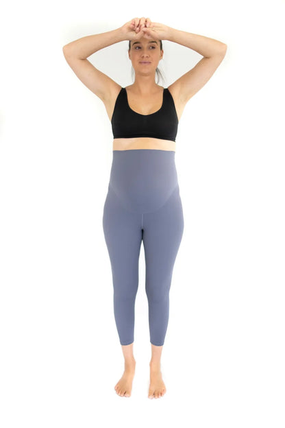 Woman in black sports bra and blue high-waisted Emamaco maternity leggings, hands on forehead