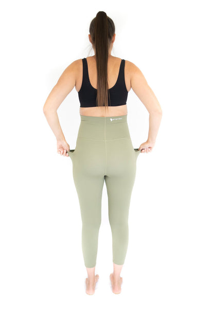 Woman in a black sports bra and sage green maternity leggings by Emamaco Maternity