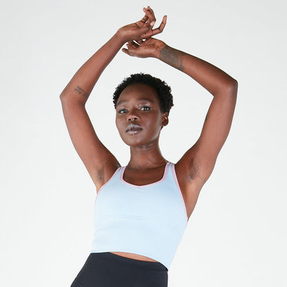 Woman in a white long line crop top poses with arms raised for maximum support