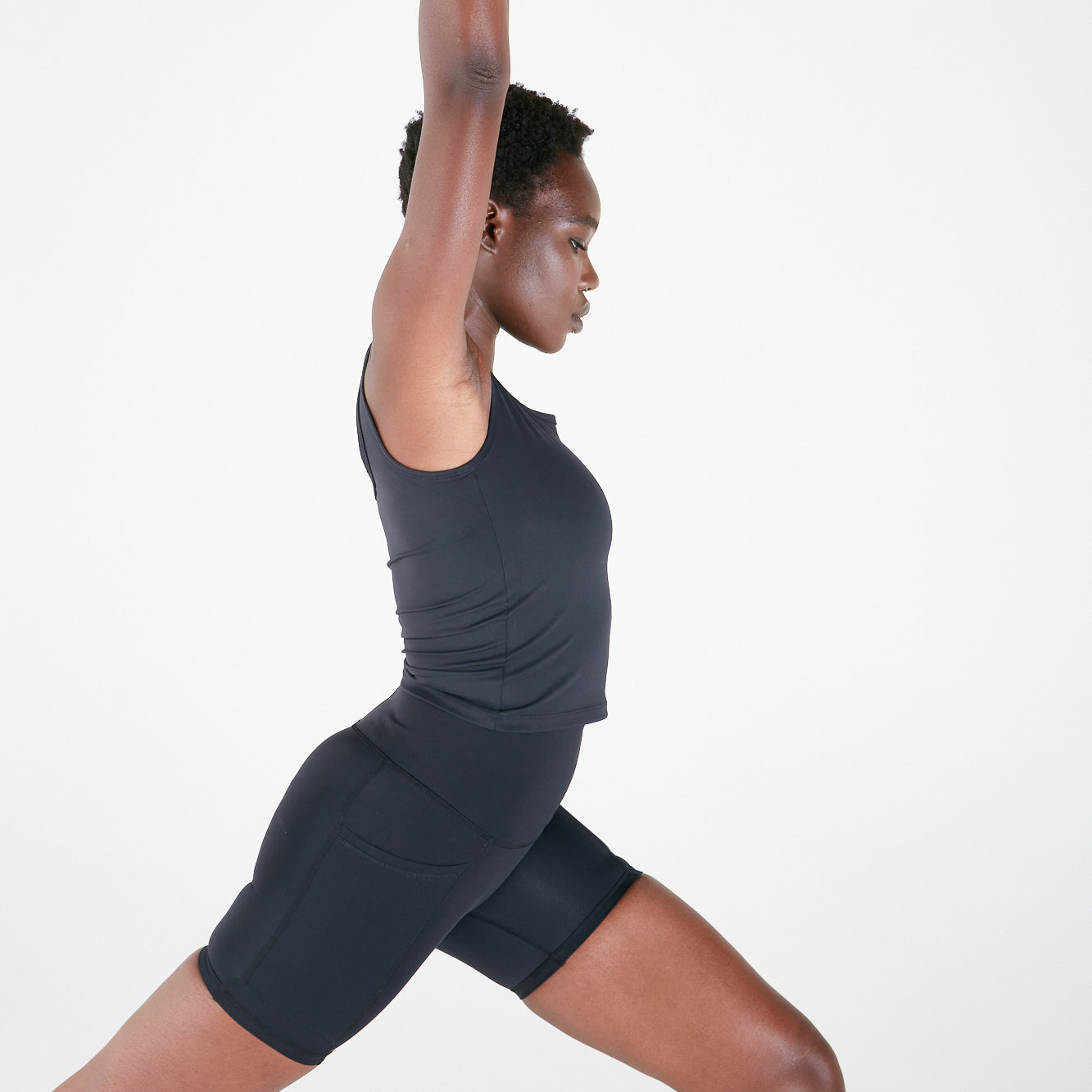 Woman in dark athletic wear stretching, showcasing Emamaco Everyday Singlet in yoga studio