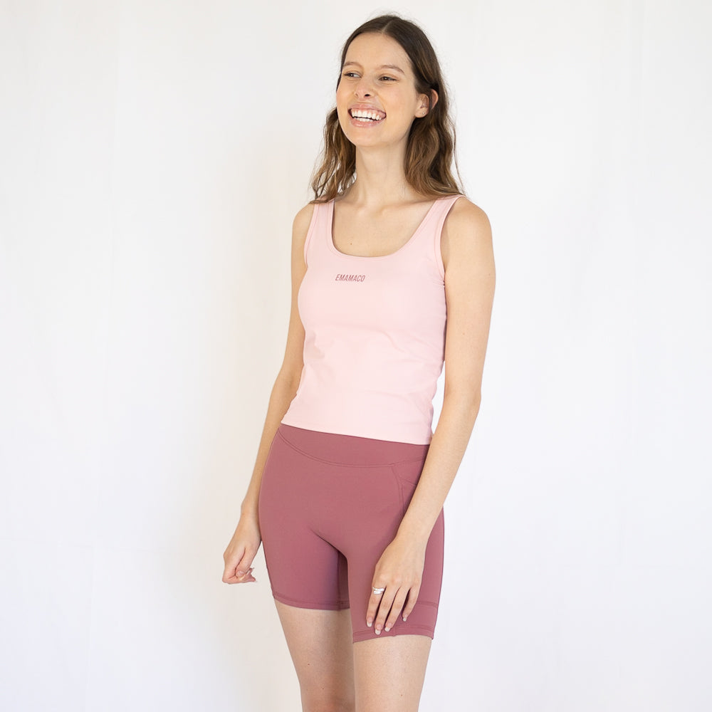 Smiling woman in pink tank top and mauve shorts, perfect for Emamaco Everyday at the yoga studio