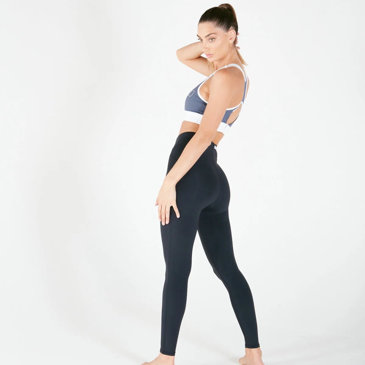 Woman in athletic wear with one hand on her neck showcasing Vibe Leggings with regular fit