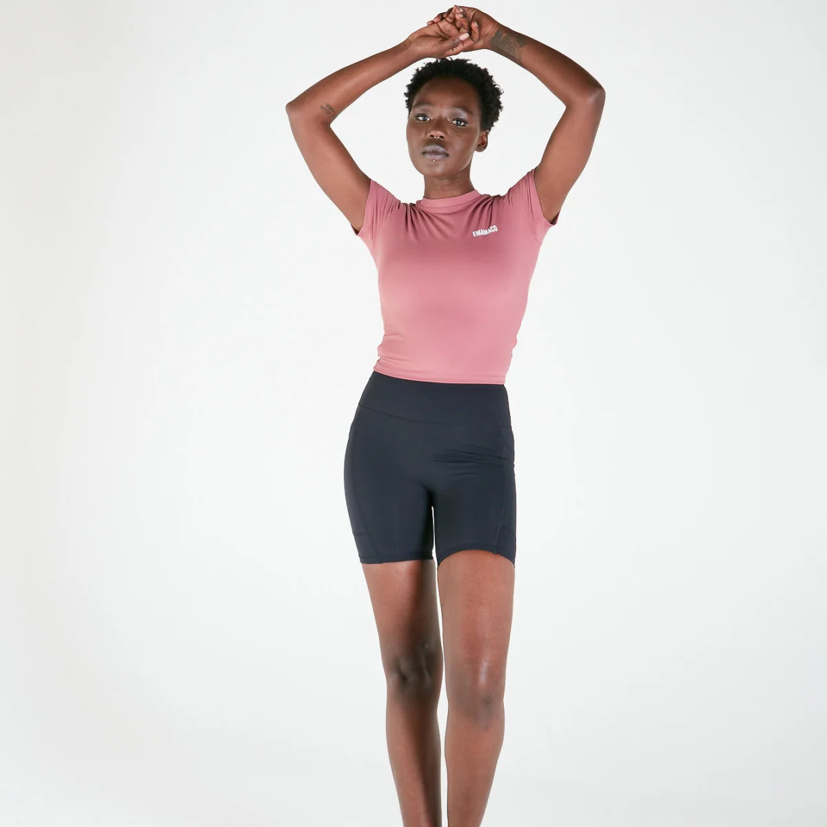 Woman in pink t-shirt and dark V-Back Bike Shorts with pockets raising arms above head